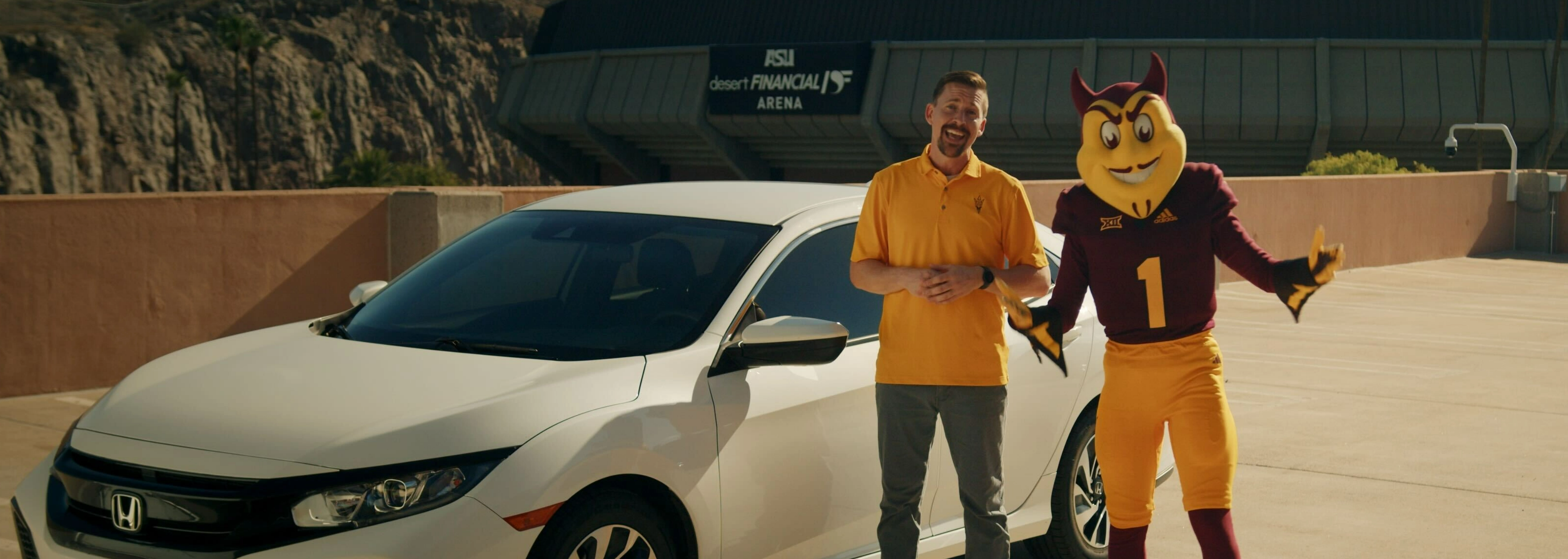 Sparky and a man wearing a gold ASU shirt standing next to a car