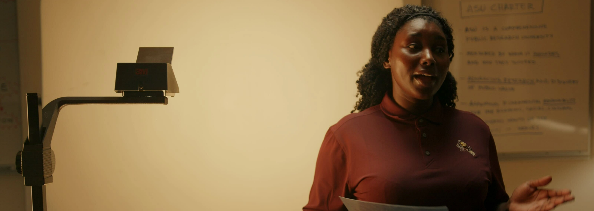 A woman wearing a maroon ASU shirt, speaking in a classroom